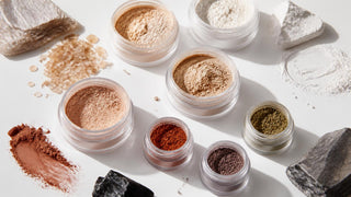 Open jars of loose mineral makeup products including foundation powder, eyeshadow pigments, and finishing powder in an editorial flat lay