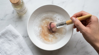 Cleaning a makeup brush in a bowl of soapy water